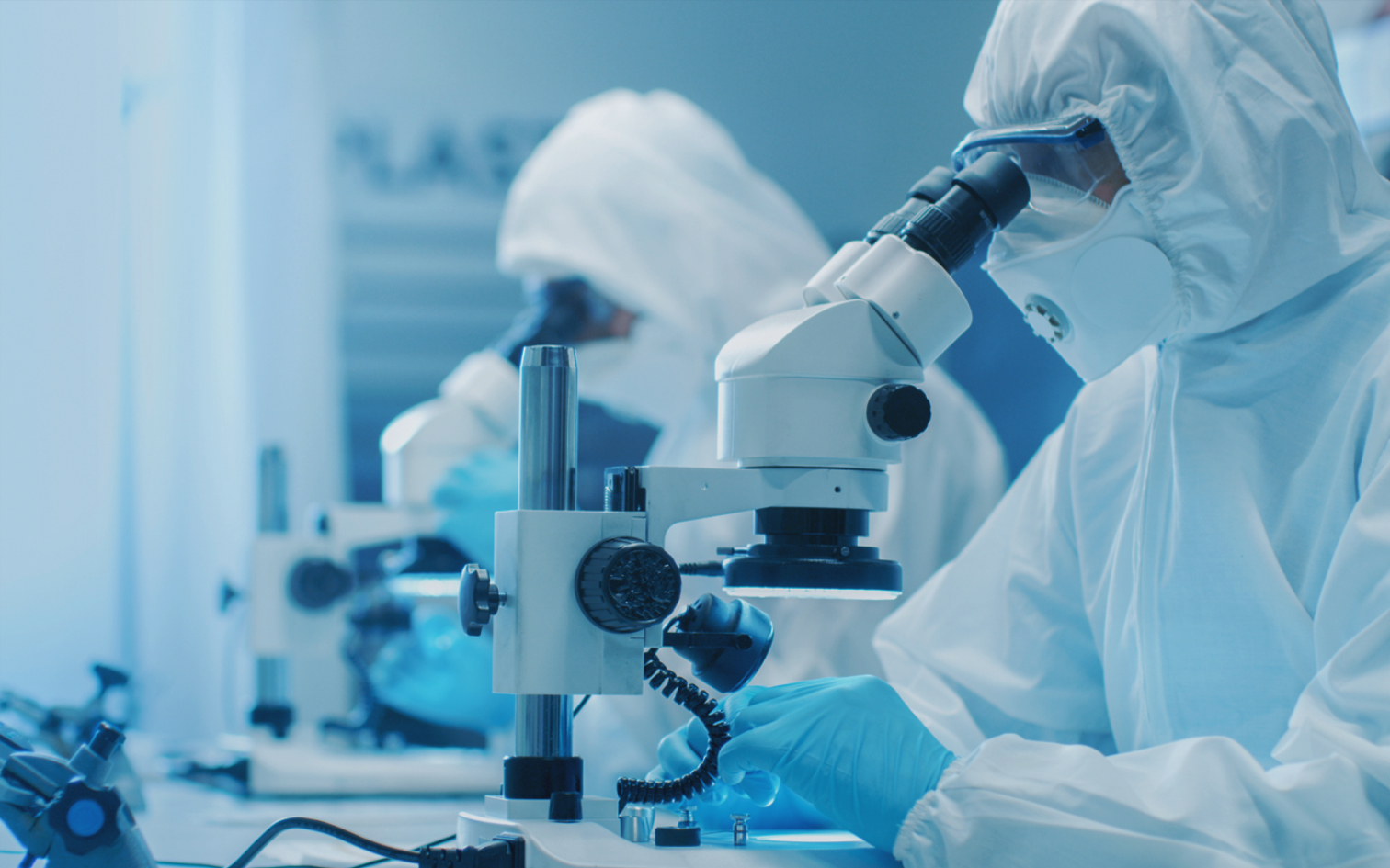 Workers in a cleanroom looking through a microscope